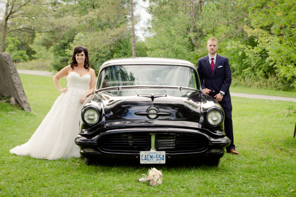 Bride and Groom standing next to a vintage car

