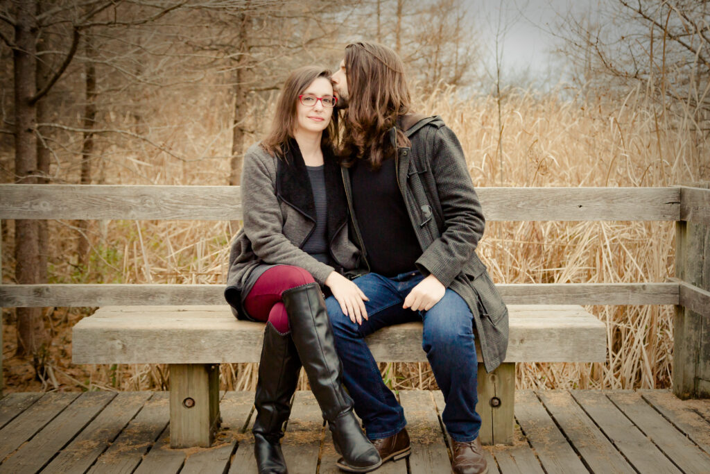 Couple seated closely on wooden bench during engagement photo session in a natural Ottawa setting